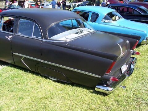 1972 Ford Ranchero - A black sedan with distinctive fins and chrome accents is parked on the grass at a car show, with a blue car visible behind it.