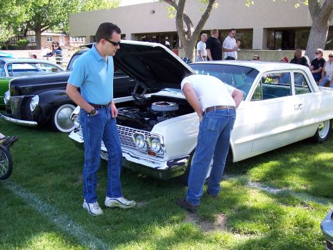 1972 Ford Ranchero - Two men examine the engine of a white sedan at a car show, with another car visible to the left.