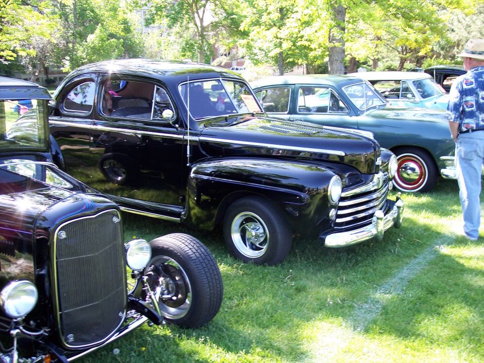 Black coupe and other cars parked on grass at a show
