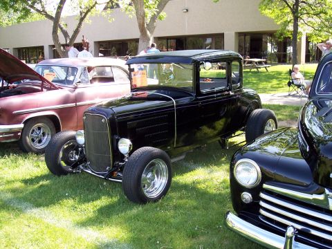 1972 Ford Ranchero - A black hot rod coupe is parked on the grass at a car show next to other classic vehicles.