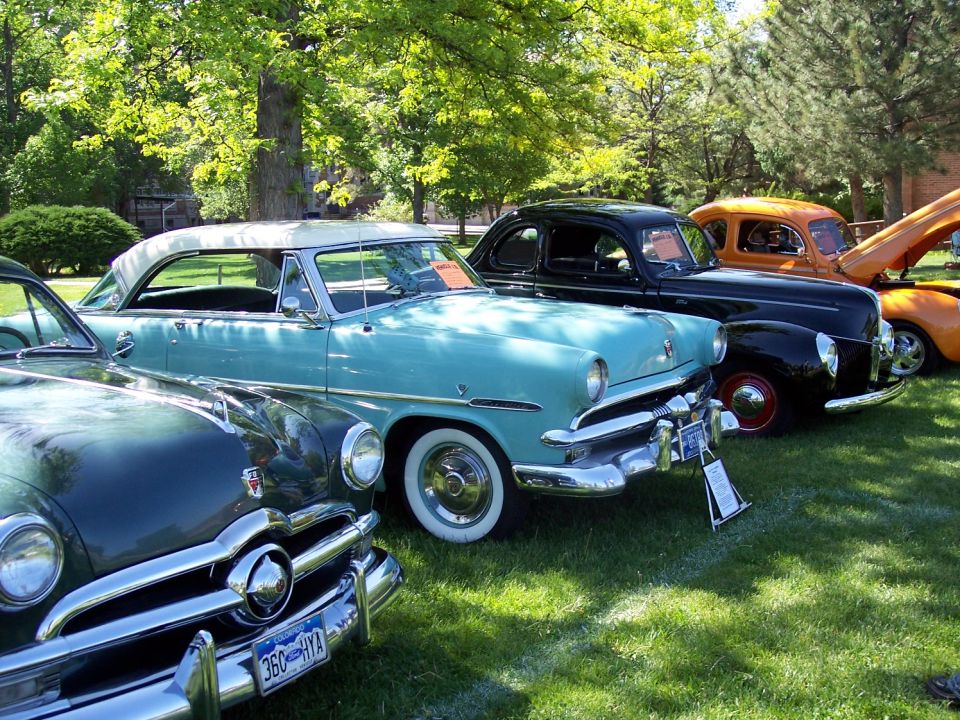 Three classic cars parked on grass, a blue one in front with a license plate reading 360-HYA