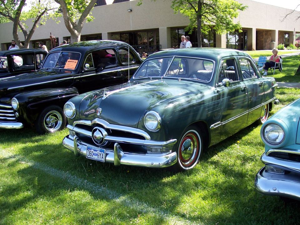 Green 1950 Ford Custom Sedan parked on grass next to a black car