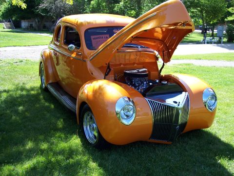 1972 Ford Ranchero - This orange hot rod coupe has its hood open, revealing the engine. A "VEHICLE I.D." sign is on the windshield.