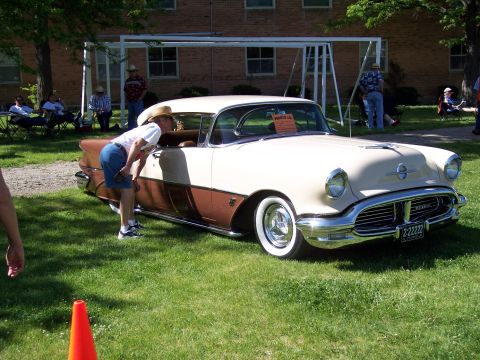 1972 Ford Ranchero - A two-tone beige and brown 1955 Oldsmobile 88 is displayed at a car show, with a person leaning in to look at the interior.