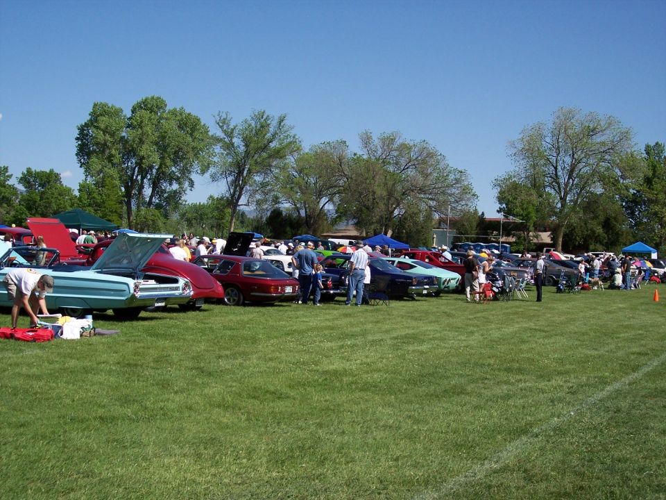 Outdoor car show with many vehicles parked on a grassy field under a clear blue sky