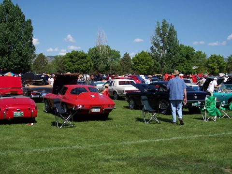 1972 Ford Ranchero - A red sports car is parked on a grassy field at an outdoor car show with other vehicles and spectators.