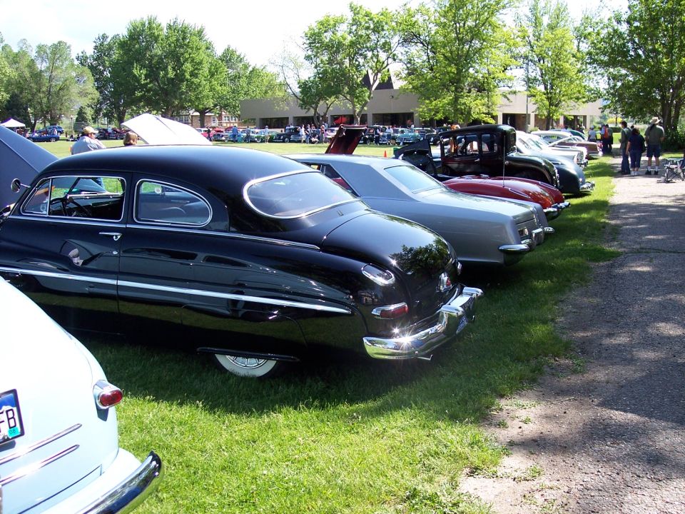 Black classic car with a rounded rear window, parked on grass