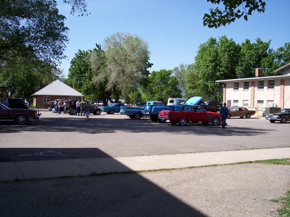 Cars parked in lot at an outdoor event, some people milling around