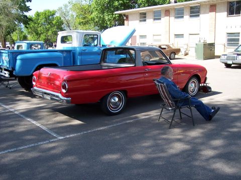 1972 Ford Ranchero - A red Ford Ranchero is parked at a car show with a man sitting in a chair nearby.