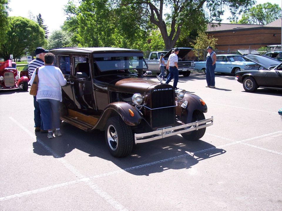Brown 1930s Dodge sedan with people looking at it. Other cars in background