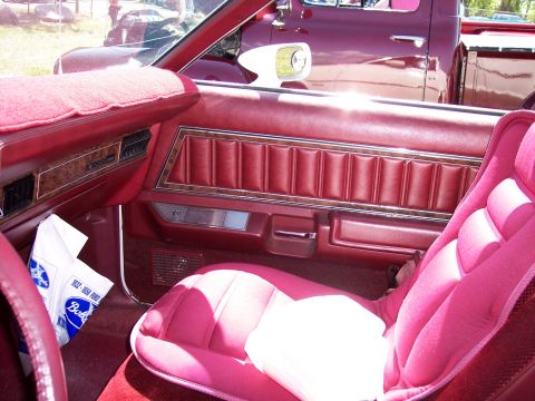 1972 Ford Ranchero - Interior view of a 1972 Ford Ranchero, showing red seats and door panels, with a pink seat cover. Another vehicle is visible outside.