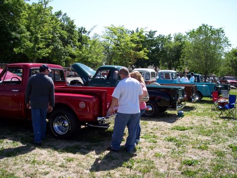 1972 Ford Ranchero - People admire various pickup trucks displayed at an outdoor event on a sunny day.