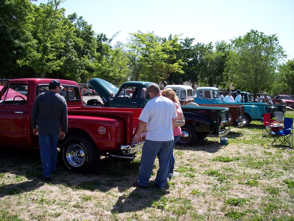 Several pickup trucks parked in a grassy lot with people milling around