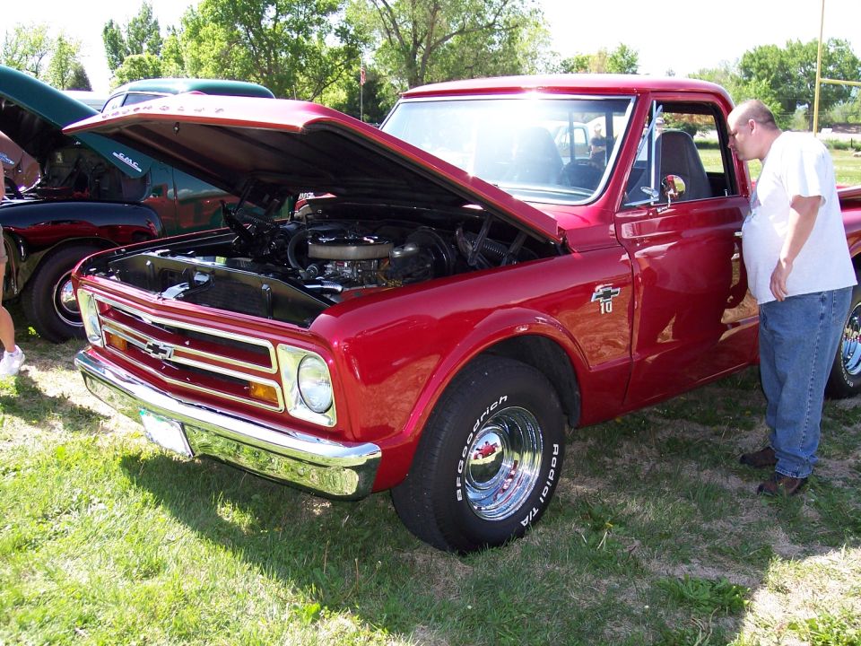 Red pickup truck with hood open, showing engine. Guy looking in door. Another car behind
