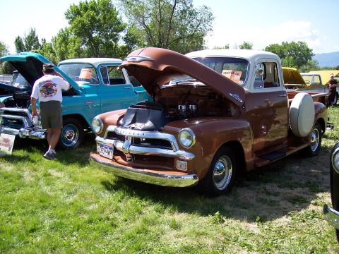 1972 Ford Ranchero - A brown and white pickup truck is displayed with its hood open at a car show, alongside other vehicles.