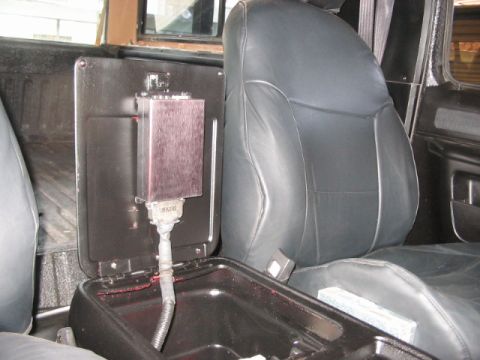 1991 Ford Bronco - The interior of a vehicle features a black leather seat and a modified center console with visible wiring and a metal enclosure.