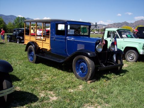 1972 Ford Ranchero - A blue vintage truck with a wooden bed is parked on a grassy field next to other vehicles under a clear sky.