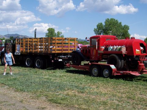 1972 Ford Ranchero - A vintage red truck with a water tank is displayed on a trailer, alongside a flatbed trailer with wooden sides.