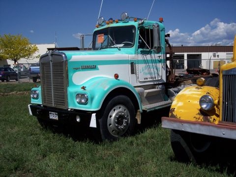 1972 Ford Ranchero - A turquoise and white Kenworth truck is parked on grass next to a yellow truck.