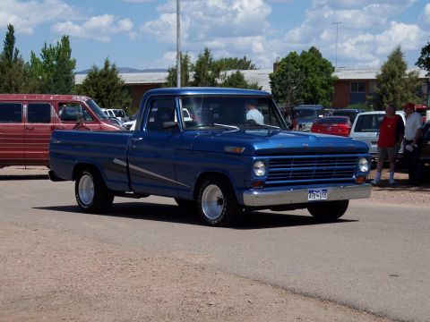 1972 Ford Ranchero - A blue pickup truck is parked outside with other vehicles and people in the background.