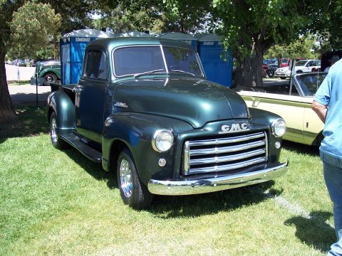 1972 Ford Ranchero - A dark green 1951 GMC pickup truck is parked on grass at a car show, with portable toilets in the background.