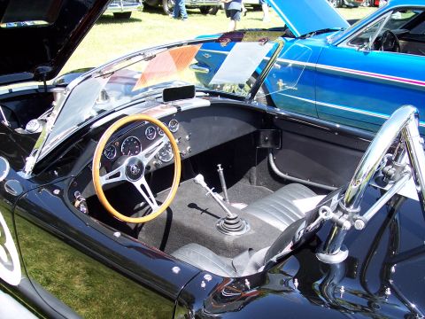 1972 Ford Ranchero - Interior view of a black convertible sports car with a wooden steering wheel and racing stripes, parked next to a blue car.