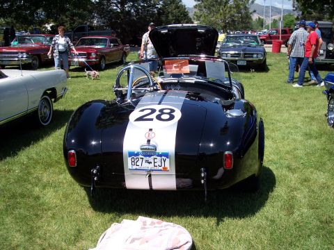 1972 Ford Ranchero - A black Shelby Cobra replica with racing stripes is parked on the grass at a car show, with other vehicles visible in the background.