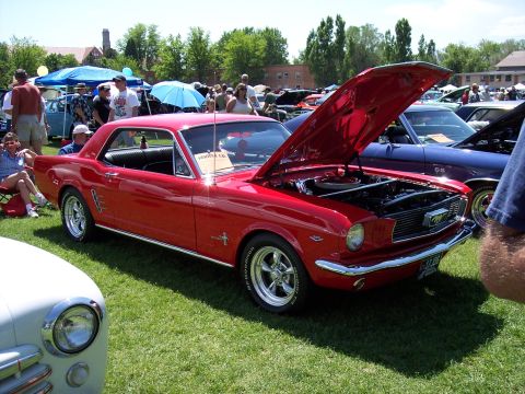 1972 Ford Ranchero - A red 1965 Ford Mustang coupe is displayed with its hood open at a car show, with other vehicles and spectators in the background.