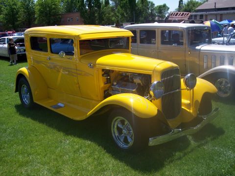 1972 Ford Ranchero - A yellow hot rod sedan with custom flames and exposed engine is displayed at a car show.