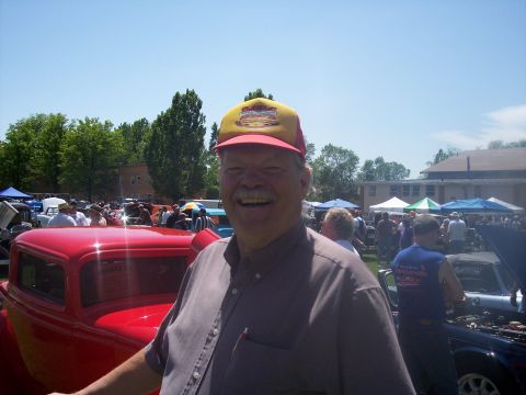 1972 Ford Ranchero - A man poses for a photo at an outdoor car show with many other vehicles and people present.