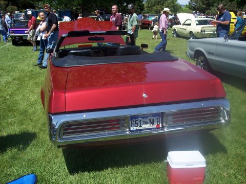 1972 Ford Ranchero - A red convertible is parked on the grass at an outdoor event with other vehicles and people around.