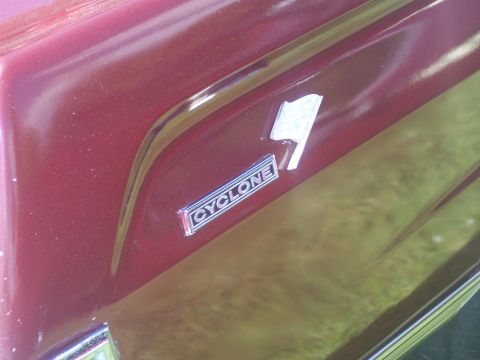 1972 Ford Ranchero - Close-up of a red car's side panel, showing the 'CYCLONE' badge and a flag emblem.