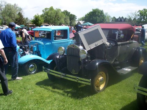 1972 Ford Ranchero - Two classic vehicles, a black convertible and a blue pickup, displayed on grass at an outdoor car show.