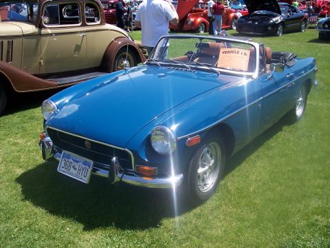 1972 Ford Ranchero - A blue convertible sports car is displayed at a car show, with other vehicles and people in the background.