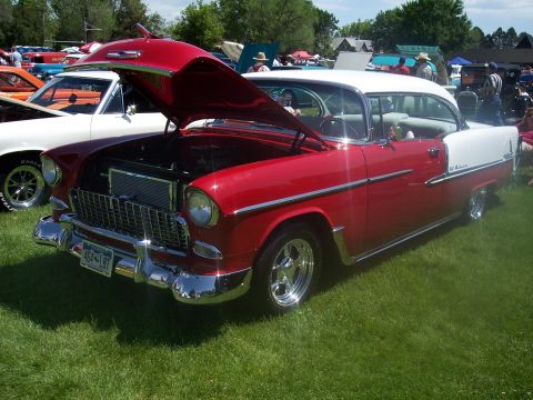 1972 Ford Ranchero - A red and white 1955 Chevrolet Bel Air is displayed at a car show with its hood open.