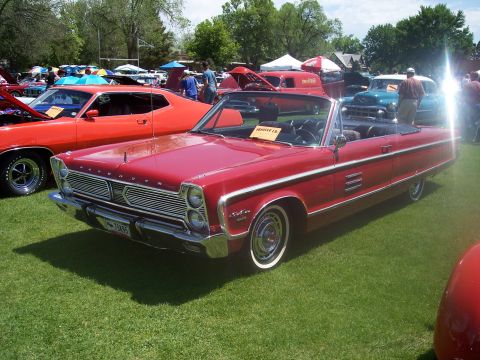 1972 Ford Ranchero - A red 1965 Plymouth convertible is displayed at a car show with other vehicles in the background.