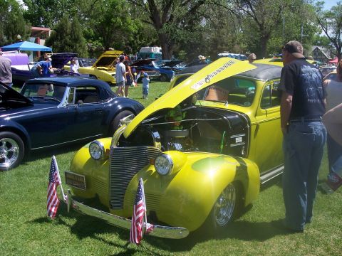 1972 Ford Ranchero - A bright yellow custom car with its hood up is displayed at a car show, with other vehicles visible in the background.