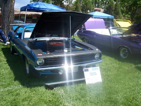 1972 Ford Ranchero - A blue 1970 Plymouth Barracuda AAR is displayed with its hood open at a car show, with other vehicles visible in the background.