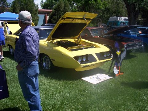 1972 Ford Ranchero - A yellow 1970 Plymouth Superbird is displayed with its hood open at an outdoor car show, accompanied by a Road Runner cutout.