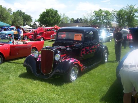 1972 Ford Ranchero - A black hot rod coupe with flame decals is displayed at a car show alongside other vehicles.