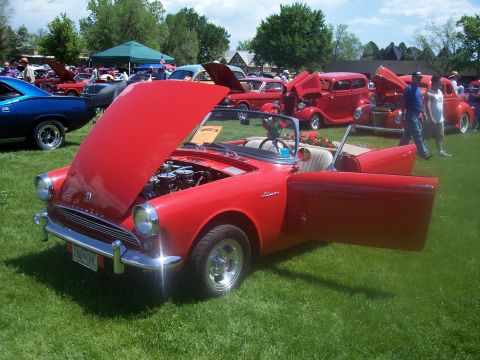 1972 Ford Ranchero - A red convertible is displayed with its hood and door open at a car show, revealing its engine and interior.
