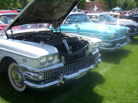 1972 Ford Ranchero - A row of classic cars are on display at an outdoor event, with the hood of the white Cadillac open.