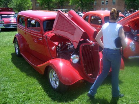 1972 Ford Ranchero - A red hot rod sedan is displayed with its hood open at an outdoor car show.