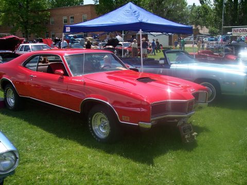 1972 Ford Ranchero - Red muscle car with hood scoop and chrome trim at a car show.