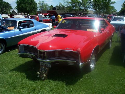 1972 Ford Ranchero - A red classic car with a hood scoop is displayed at an outdoor car show.