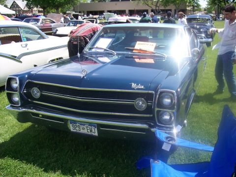 1972 Ford Ranchero - A dark blue 1967 AMC Marlin is displayed at a car show, with other vehicles and tents in the background.