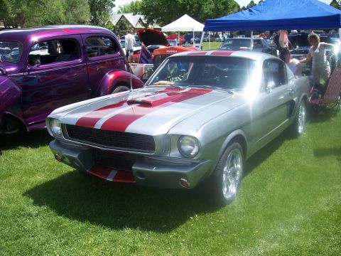 1972 Ford Ranchero - A silver 1965 Ford Mustang with racing stripes is displayed at an outdoor car show.