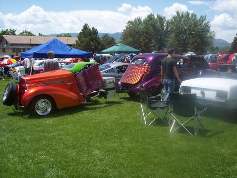 1972 Ford Ranchero - A custom orange coupe with a spare tire and a checkered flag is displayed at a car show alongside other vehicles.