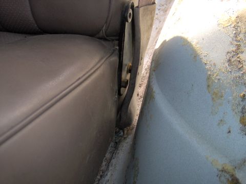 1993 Ford Bronco - The interior of a vehicle shows a close-up view of the door hinge mechanism and the edge of a seat.