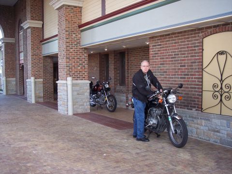1985 Ford LTD Crown Victoria - A man sits on a motorcycle in front of a brick building, with another motorcycle parked behind him.